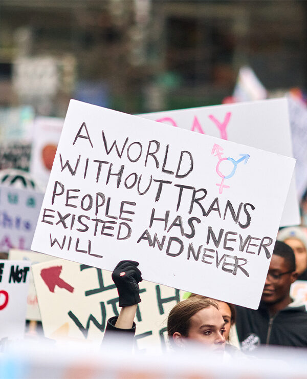 A pesron holding up a sign reading "A World Without Trans People Has Never Existed And Never Will" at a demonstration.
