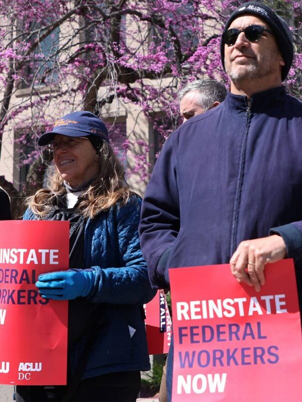 Rally where people are holding signs that say "Reinstate Federal Workers Now"