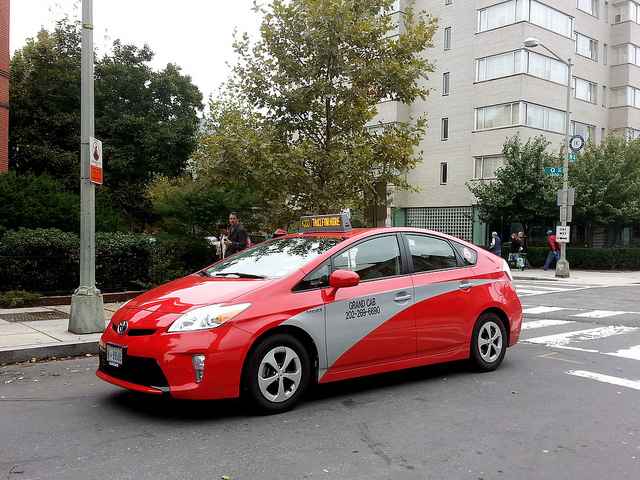 Image of a red taxicab with a silver accent on a D.C. street corner