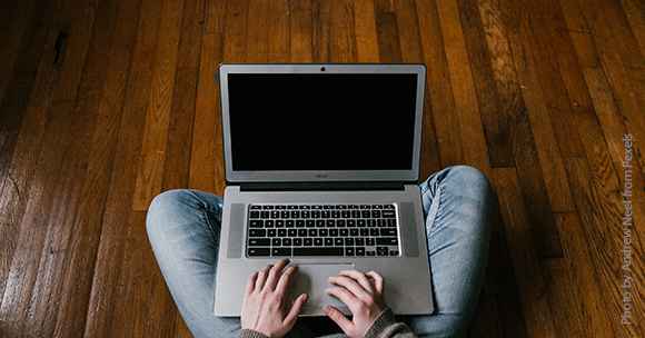 picture of person in jeans sitting cross-legged on floor with laptop