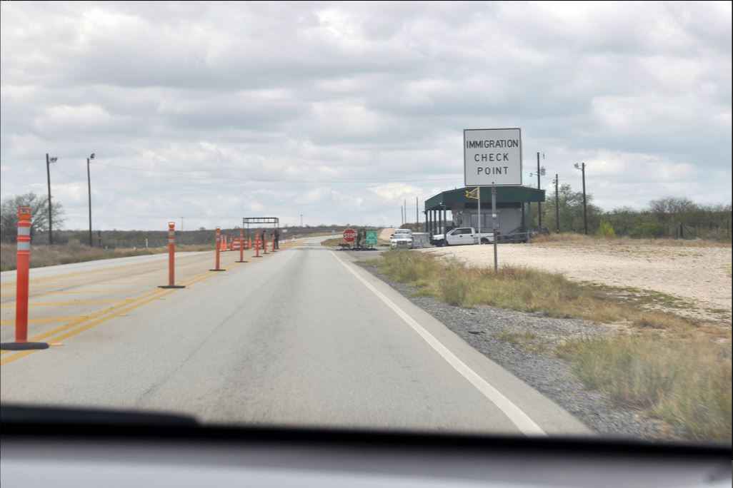 Image description: view from the dashboard of a car approaching a sign stating "immigration check point" in a desert landscape