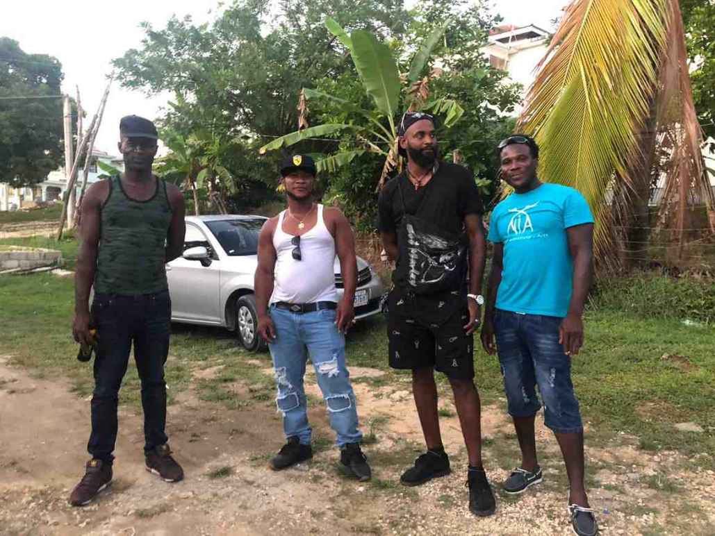 Image description: Plaintiffs Robert Dexter Weir, Patrick Wayne Ferguson, David Roderick Williams, and Luther Fian Patterson are next to each other. They are surrounded by lush jungle greenery and stand in front of a white car.