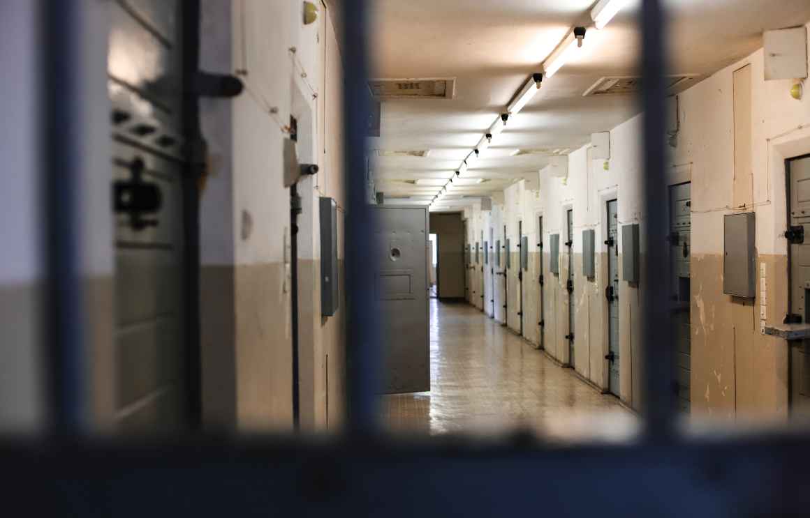ID: a grim and foreboding view down a detention center's corridor through the bars of a cell. 
