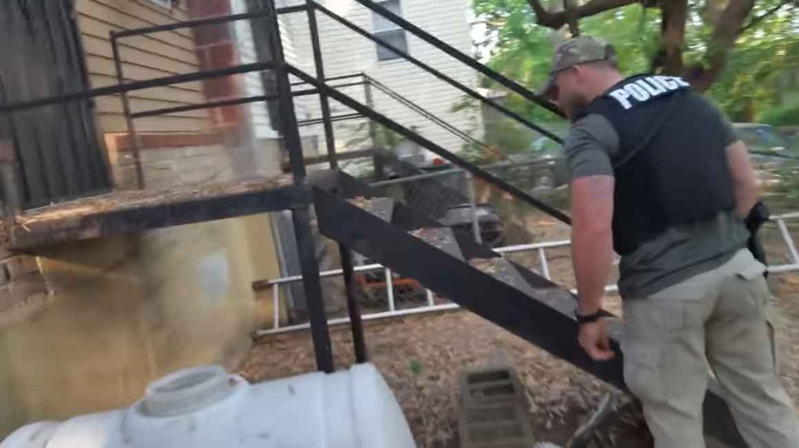 image description: MPD Officer Gupton conducts a warrantless search of our client Ms. Price's home. In the picture, he stands to the right of the frame and peers at the side of Ms. Price's house. End description.