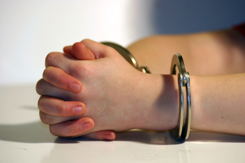 Image description: close up of a light-skinned juvenile's hands which are cuffed and resting on a table