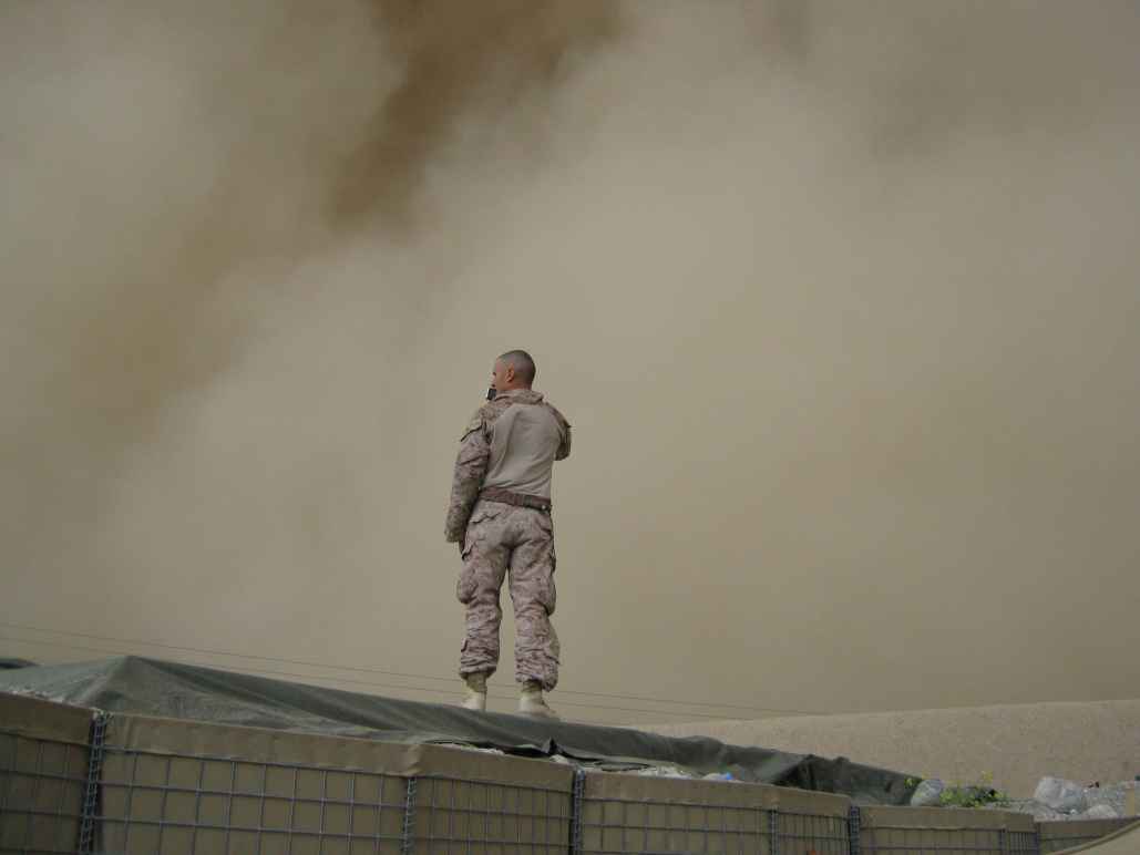 Soldier in fatigues standing on a structure against a dusty brown backdrop