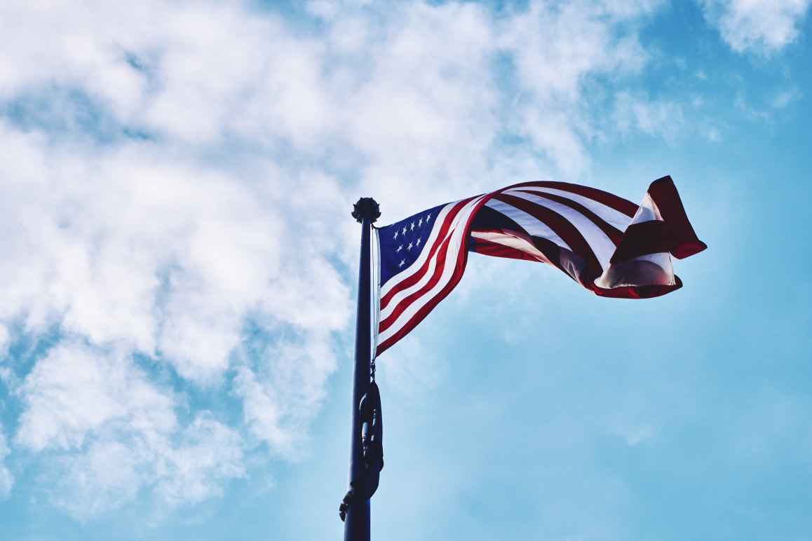 American flag waving with blue sky and light clouds in the background