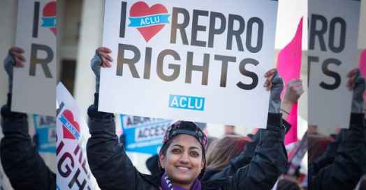 Smiling person holding an "I heart Repro Rights" sign