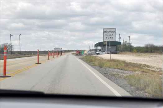 Image description: view from the dashboard of a car approaching a sign stating "immigration check point" in a desert landscape